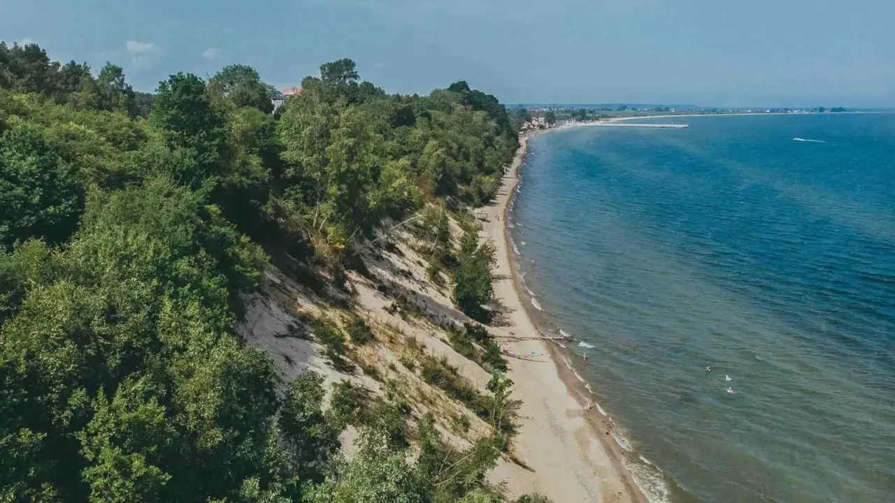 Malownicza plaża Mechelinki z zielonymi klifami i turkusowym morzem. Kilka osób odpoczywa na piasku, inni kąpią się w wodzie.