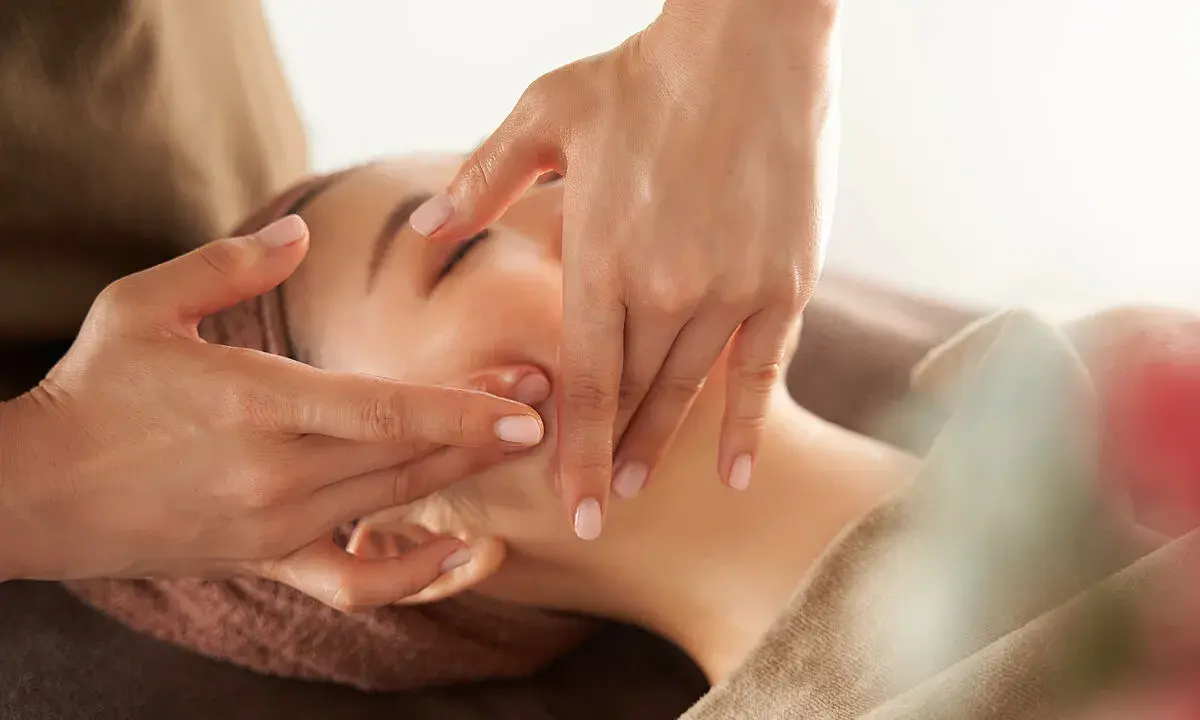 Manos expertas realizan un **dibujo masaje facial paso a paso**, aplicando suaves presiones en el rostro de una mujer para relajarla.