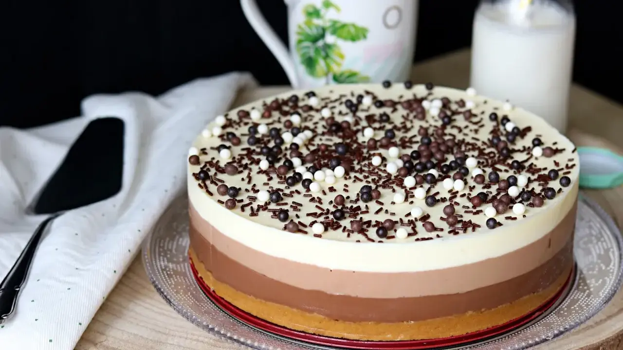 Deliciosa tarta de tres chocolates, con capas de blanco, con leche y negro, cubierta de virutas y bolitas de chocolate.