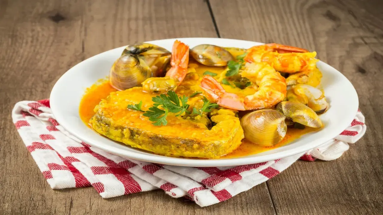 Plato de comida asturiana con un trozo de pescado, gambas y almejas en salsa.