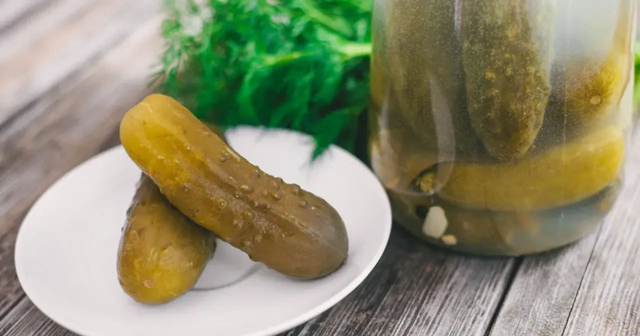 Dwa ogórki kiszone na talerzyku, obok słoik pełen kiszonków. Zastanawiasz się, dlaczego ogórki kiszone są puste w środku? To proces fermentacji!