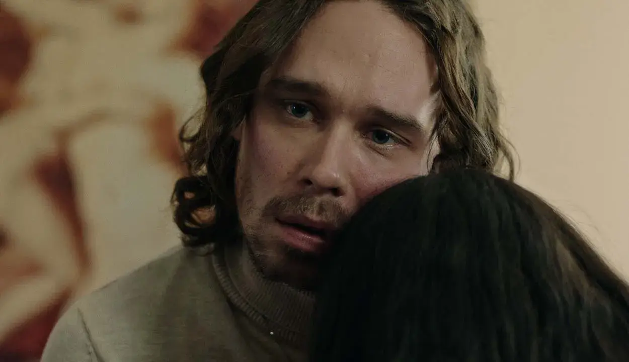 En man med långt hår och blå ögon kramar någon i tv-serien "Knutby".