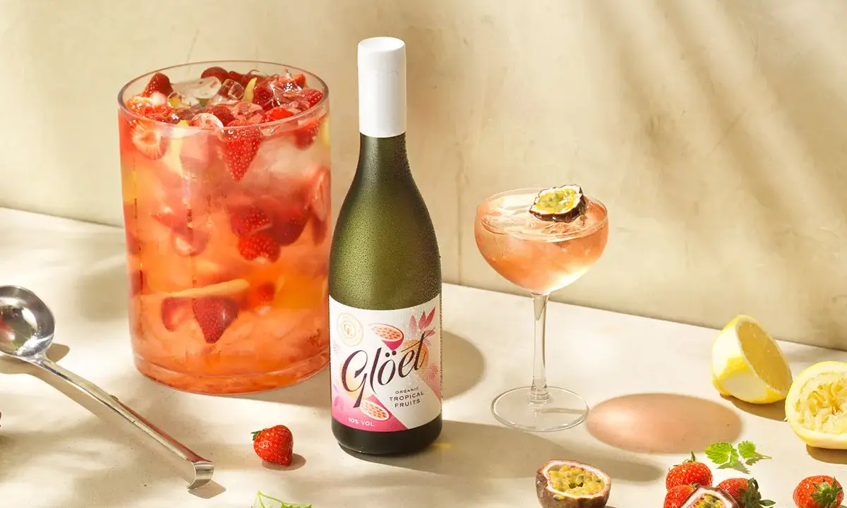 En stor bålskål fylld med jordgubbar och is, en flaska vitt vin och en cocktail med passionsfrukt. Perfekt för en somrig drink med vitt vin.