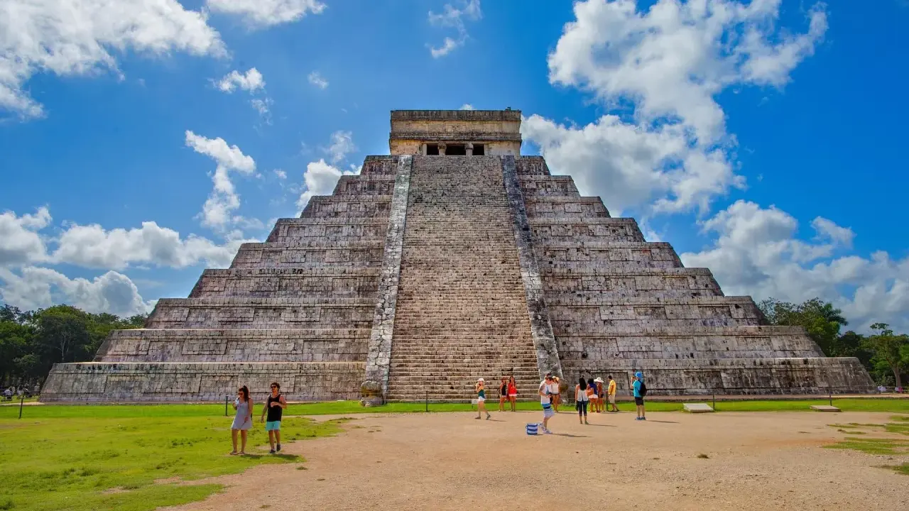 Majestatyczna piramida w Chichen Itza, z turystami podziwiającymi jej piękno na tle błękitnego nieba.