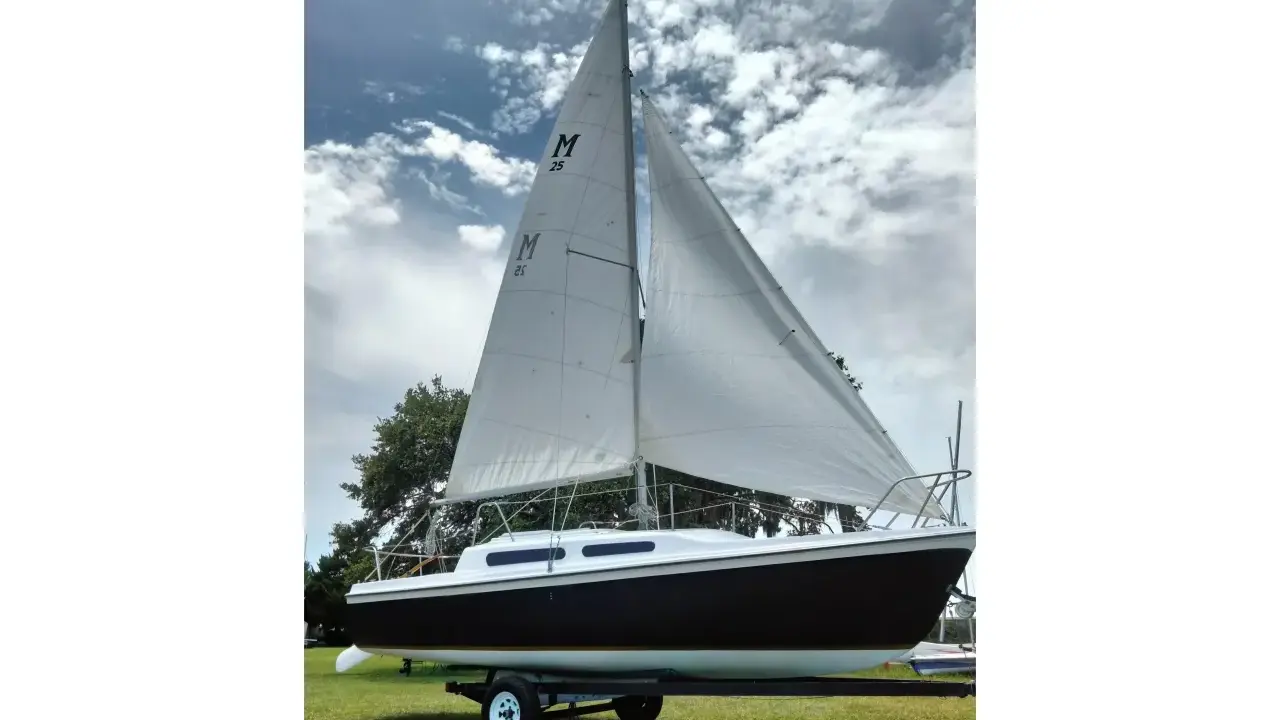 Voilier Mac Gregor 25, prêt à naviguer, avec ses voiles blanches gonflées par le vent sous un ciel nuageux.