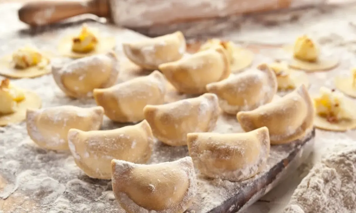 Gotujesz pierogi? Zobacz, jaka mąka do pierogów będzie najlepsza! Na zdjęciu świeżo lepione pierogi, wałek i rozsypana mąka.