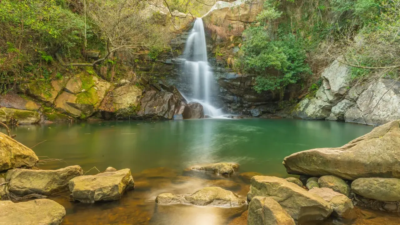 Cascada en un entorno verde con aguas cristalinas, evocando la belleza de las piscinas naturales de Cádiz.