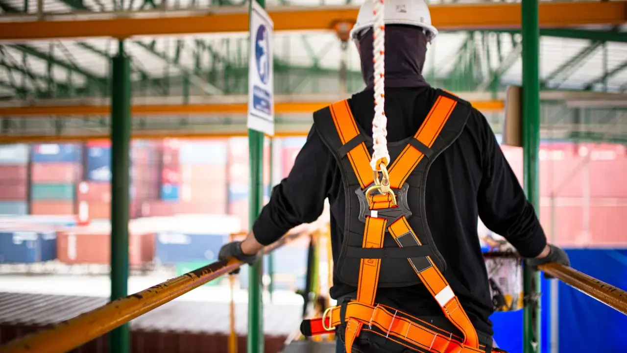 Trabajador con arnés de seguridad naranja y blanco, listo para trabajar en altura. La vida útil de un arnés de seguridad depende de su uso y mantenimiento.