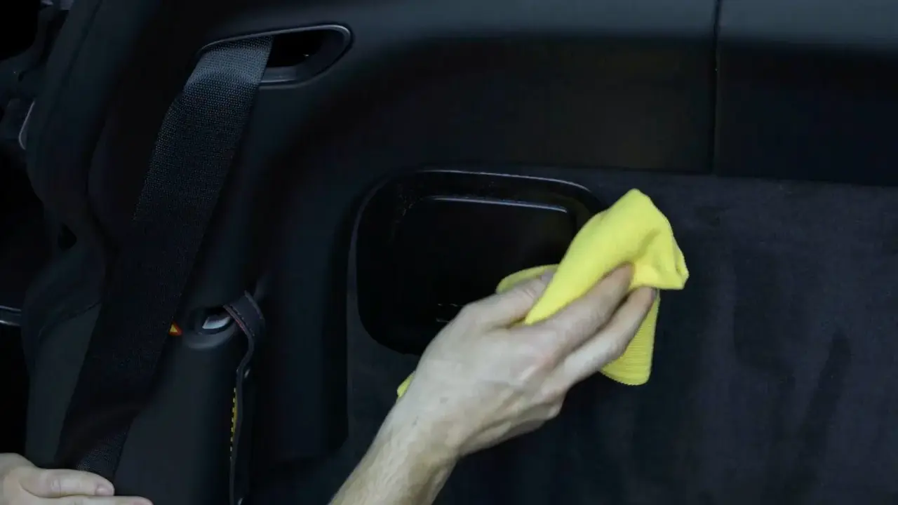 Hand wischt mit gelbem Tuch über schwarzes Kunstleder im Auto. So einfach ist Kunstleder reinigen.