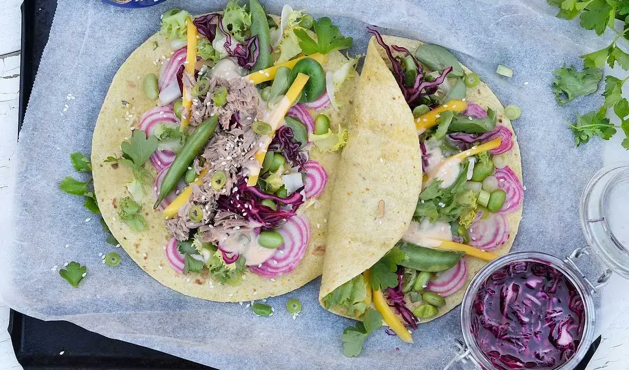Två läckra tonfisk wraps fyllda med grönsaker, rödlök och en krämig sås. En burk med rödkålssallad står bredvid.