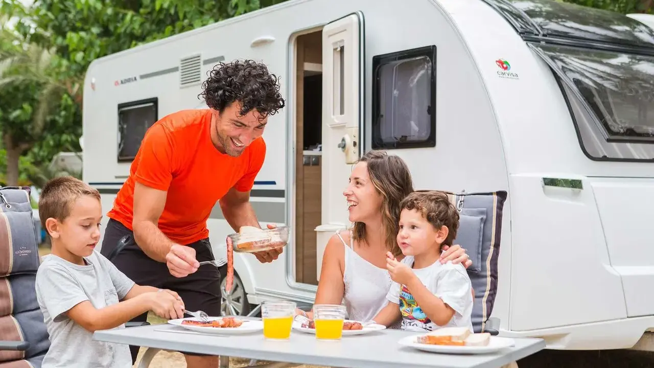 Familia disfrutando de un picnic en campamentos para familias, con una caravana de fondo.