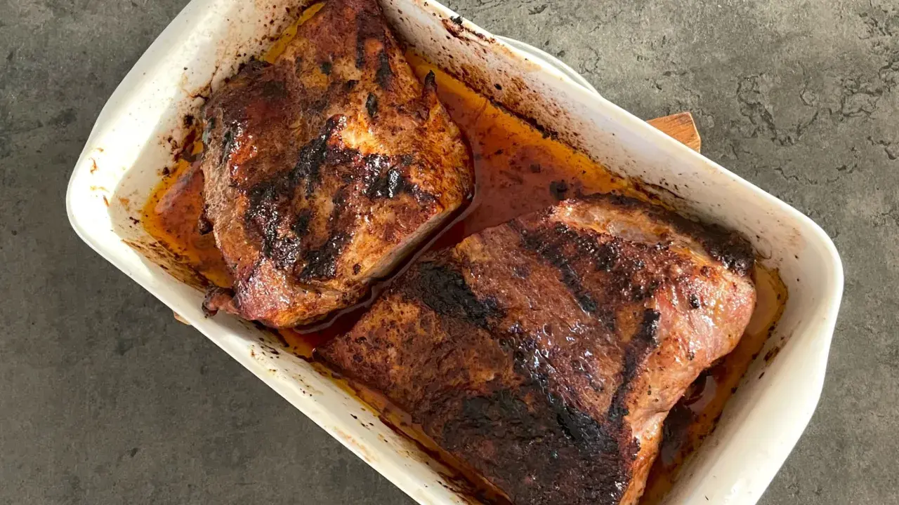Två saftiga bitar av grillad pluma ligger i en vit ugnsform, redo att serveras.