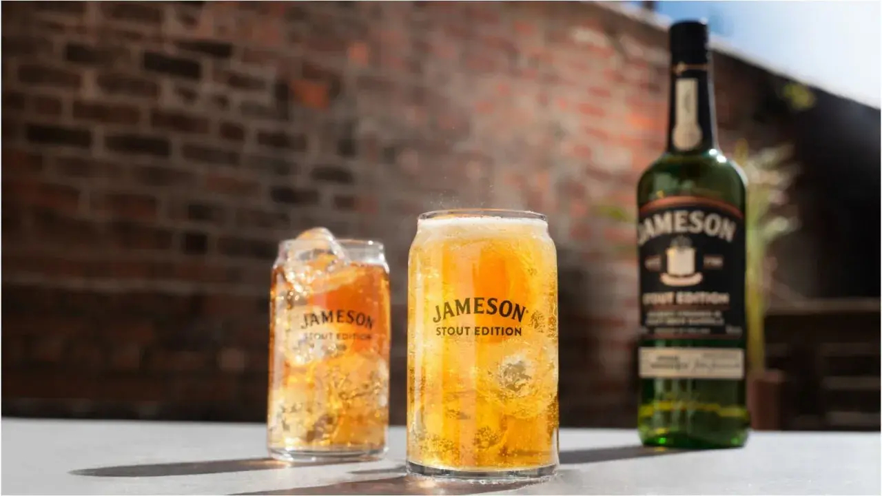 Dwa orzeźwiające drinki z lodem i butelka Jameson Stout Edition na tle ceglanej ściany.