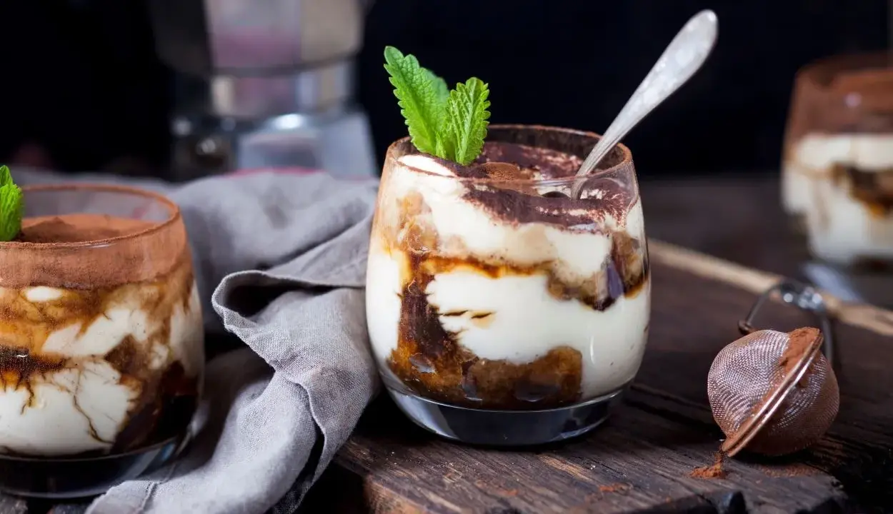 Pyszne tiramisu w pucharkach, udekorowane listkiem mięty, na drewnianej desce.
