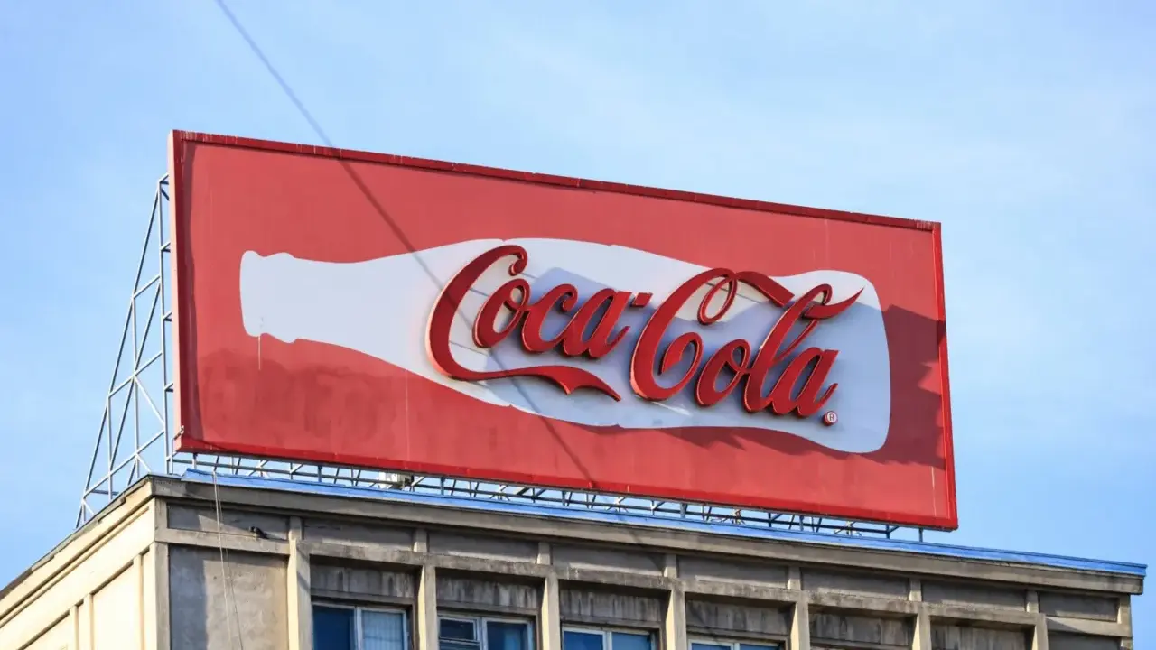 Duży baner logo Coca-Cola na dachu budynku, z charakterystyczną białą butelką i czerwonym napisem.
