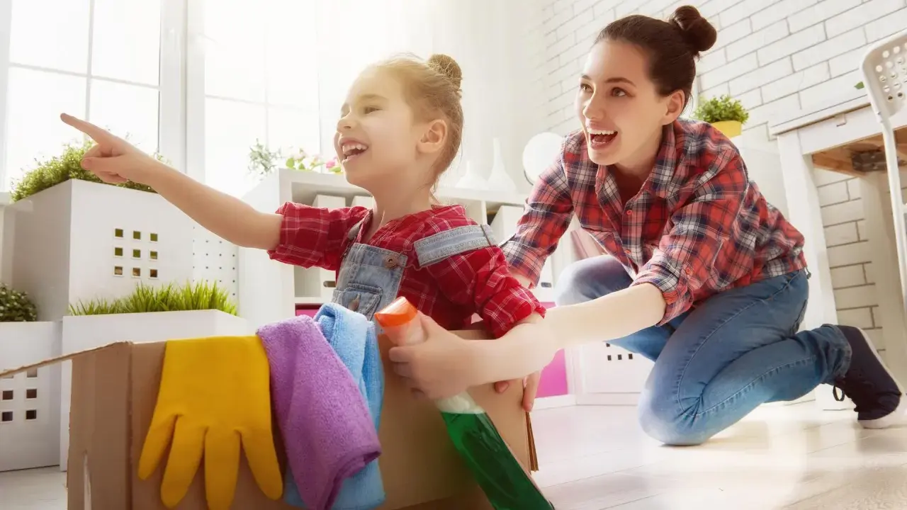 Mama i dziecko bawią się w sprzątanie, ucząc się jak nauczyć dziecko sprzątać. W kartonie są rękawice i płyn.