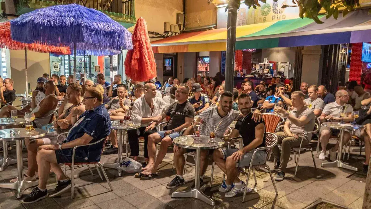 People enjoying drinks at outdoor tables outside gay bars in Sitges, Spain.