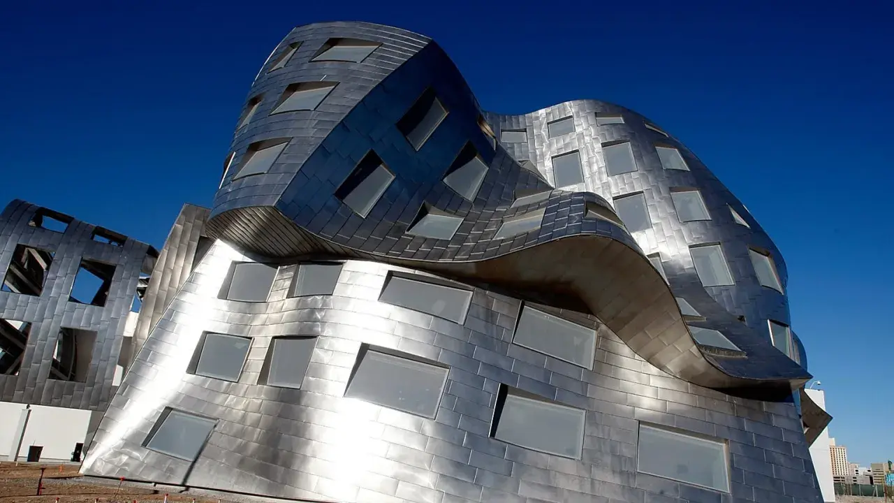 Edificio dalle forme ondulate e metalliche, una delle opere di Frank Gehry, con finestre quadrate e rettangolari.