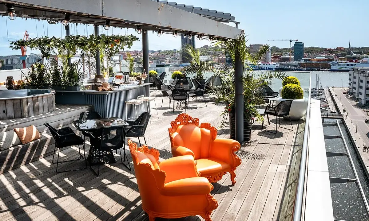 Solig rooftop bar i Göteborg med orangea fåtöljer och utsikt över hamnen.