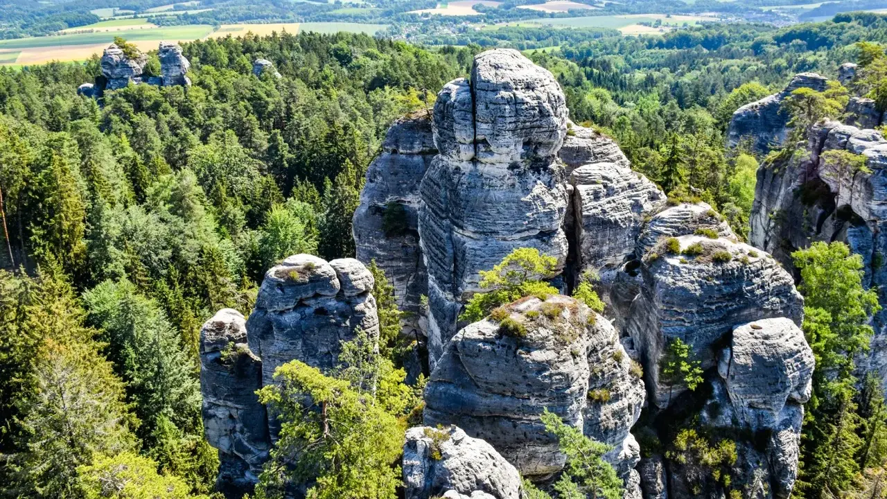 Majestatyczna, hruba skala wznosi się pośród gęstego lasu. W oddali widać pagórkowaty krajobraz.