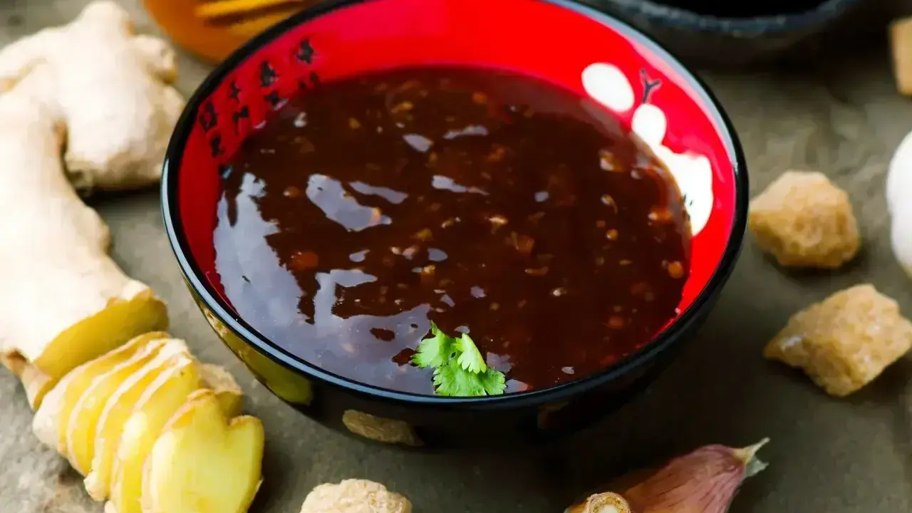 Sos teriyaki przepis: miseczka pełna aromatycznego sosu, obok świeży imbir, czosnek i brązowy cukier. Idealny do dań azjatyckich.