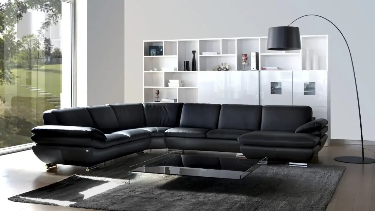 Sofá modular negro de cuero, con mesa de centro de cristal y estanterías blancas. Un diseño de gran dimensión.