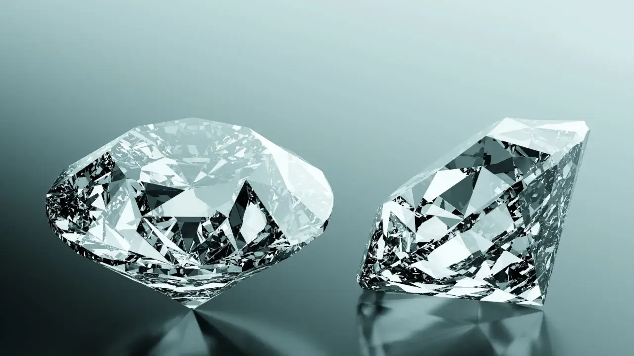 Due diamanti scintillanti, uno rotondo e uno a goccia, riflettono la luce. Uno dei due, un diamante brown, brilla con sfaccettature perfette.