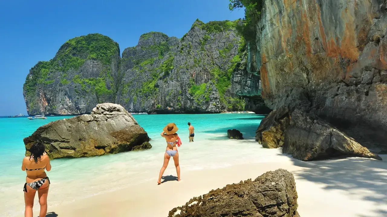 Två personer njuter av det turkosa vattnet och de dramatiska klipporna vid Maya Bay, Thailand.