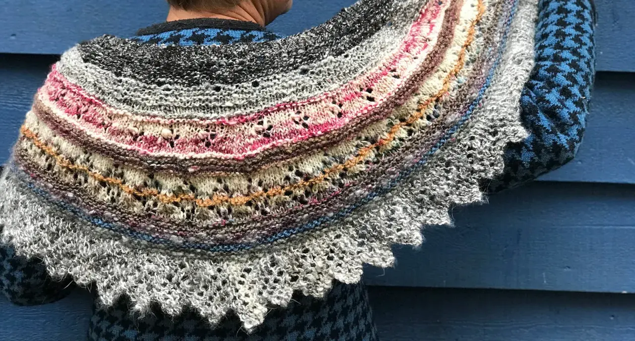Un chal de lana tejido con hilos de colores, con un intrincado diseño de encaje y bordes festoneados. Los mantoncillos de crochet son una obra de arte.