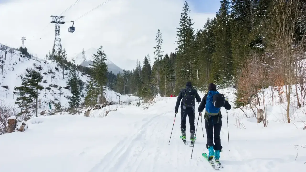 Dwie osoby na skitury w Tatrach, w tle kolejka linowa i ośnieżone drzewa.