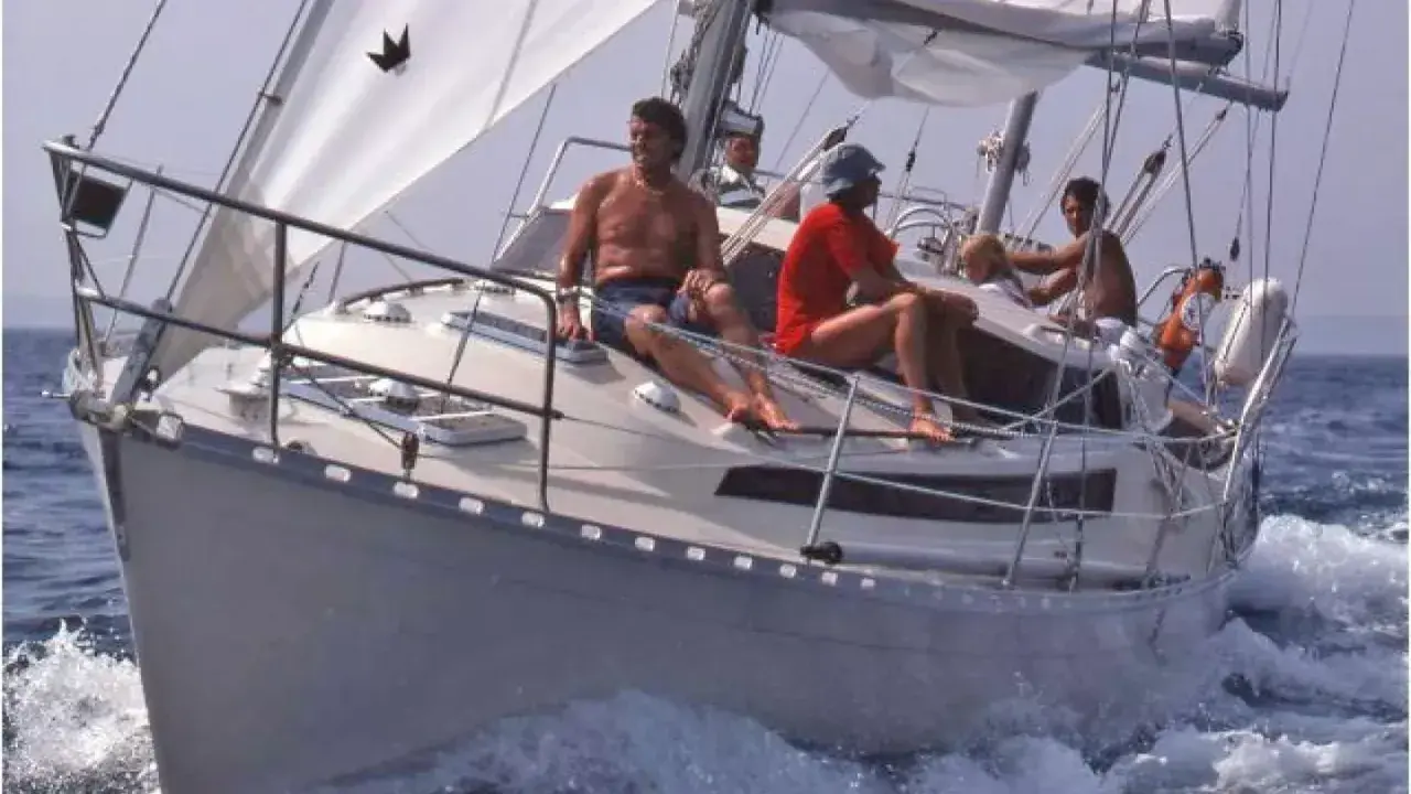 Un groupe profite d'une journée en mer sur ce qui semble être le meilleur voilier fifty, naviguant sur des eaux bleues avec des voiles blanches gonflées par le vent.
