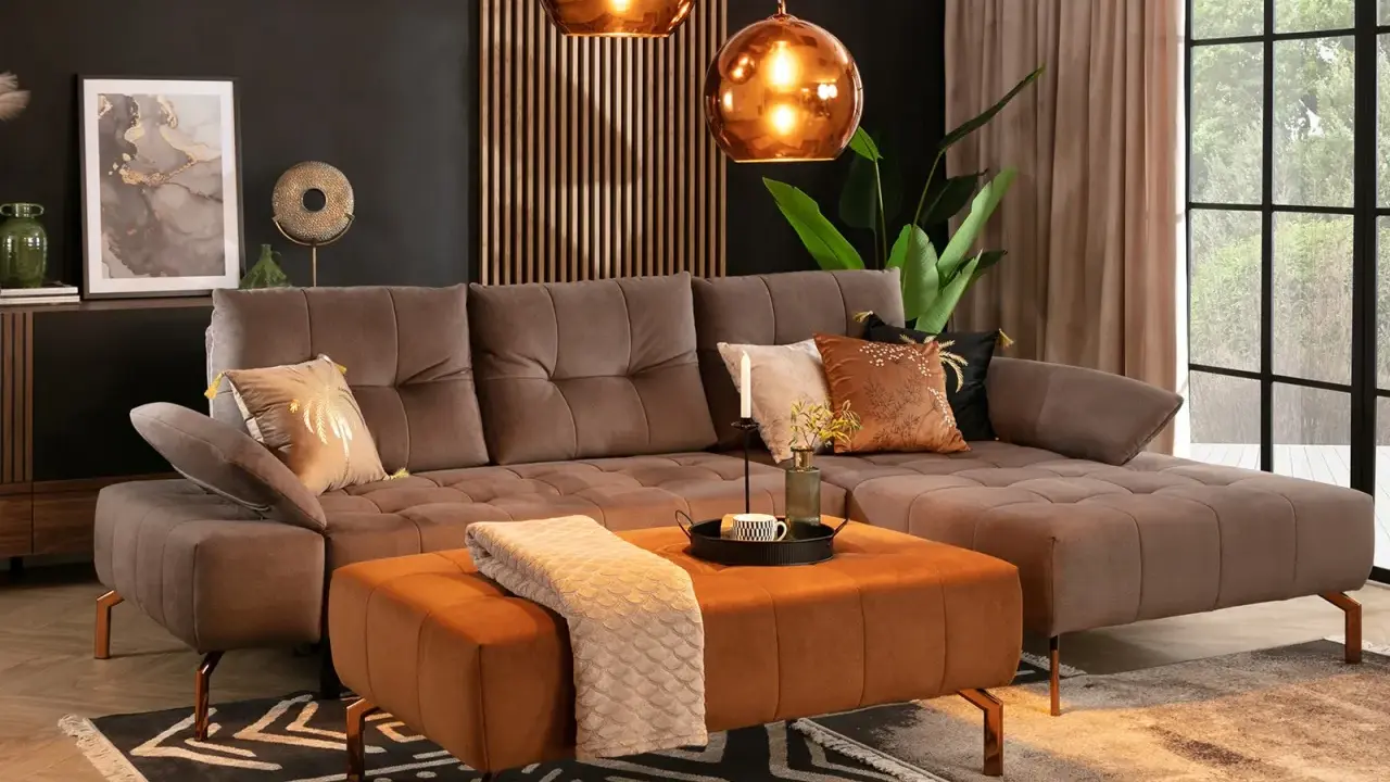 Elegancki salon z sofą w kolorze taupe. Idealnie komponuje się z pomarańczowym pufem, miedzianymi lampami i złotymi dodatkami.
