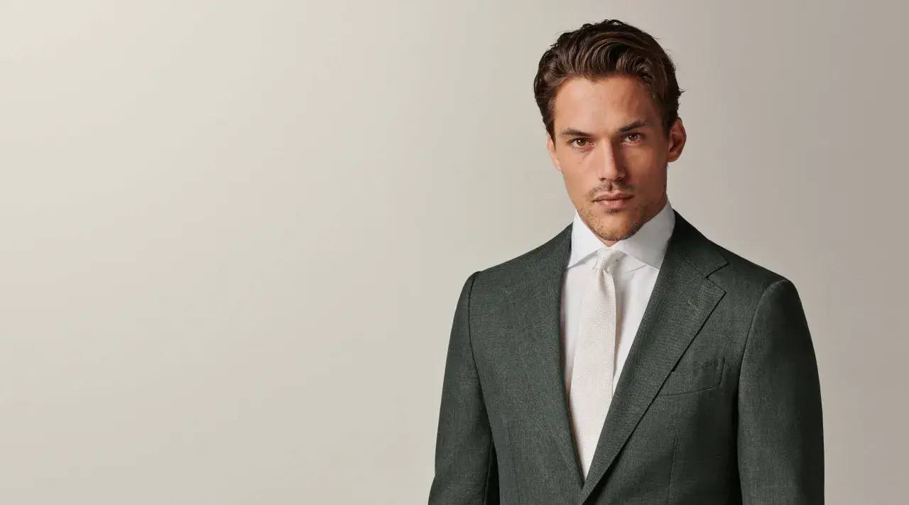 A man in a dark green suit and white shirt with a cream tie. This timeless look embodies the perennial suit meaning of enduring style and sophistication.