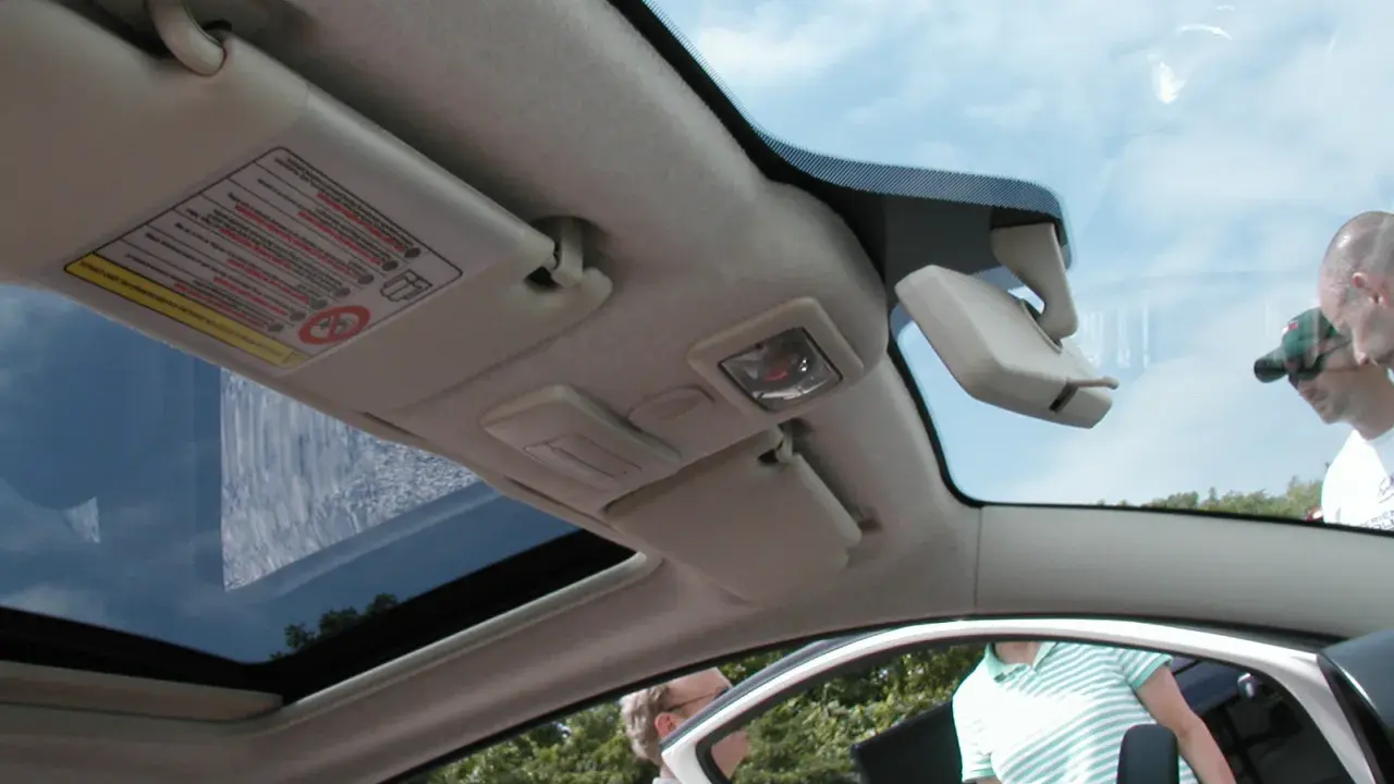 Interior de un Fiat 500 con el techo solar abierto, mostrando el parasol y el espejo retrovisor.