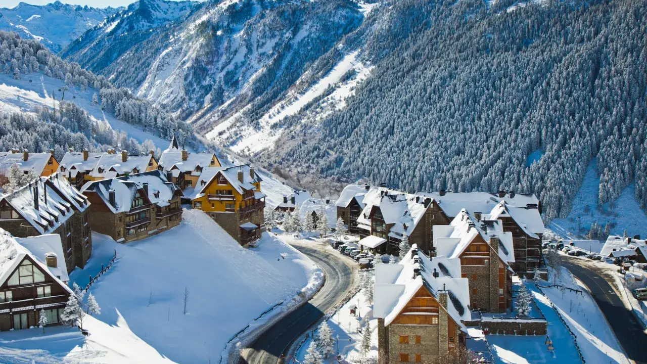 Pueblo nevado en los Pirineos, ideal para saber donde ir en el puente de diciembre. Casas de piedra y madera cubiertas de nieve, rodeadas de bosques y montañas.