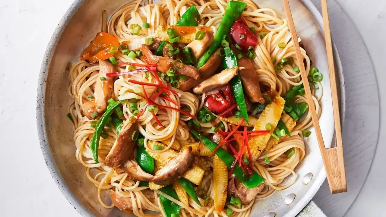 Pyszny makaron sojowy z kurczakiem, warzywami i papryczką chili, podany w metalowej patelni z pałeczkami.