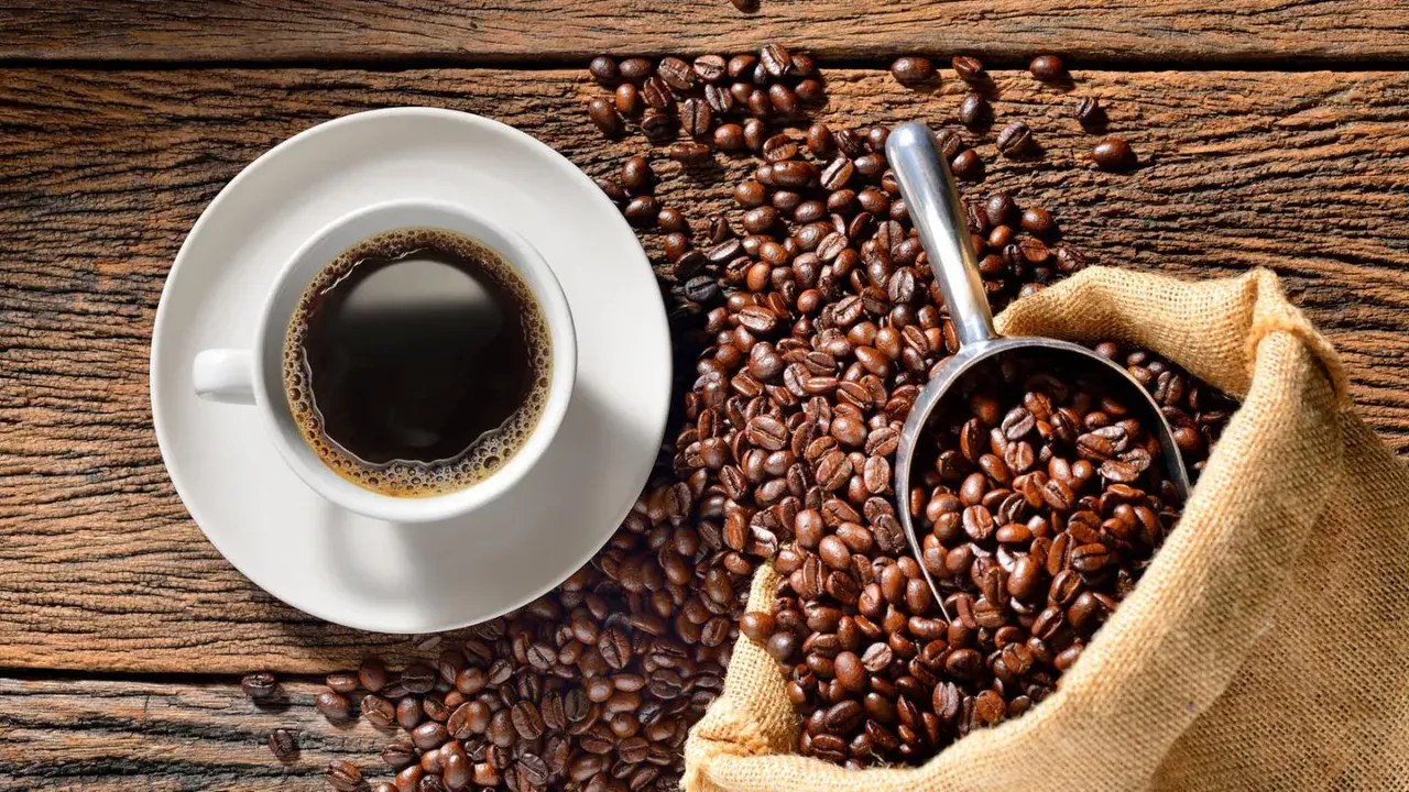 Eine Tasse heißer Kaffee neben einer Schaufel voller gerösteter Bohnen und einem Jutesack. Der Duft von perfekt gebrühtem Filterkaffee liegt in der Luft.