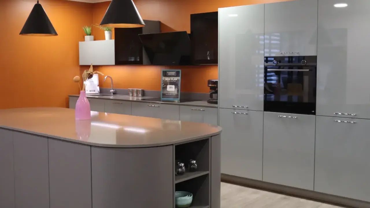 Cuisine moderne avec îlot central et armoires grises. Les murs orange vif contrastent avec les surfaces épurées, créant une ambiance chaleureuse. Une cuisine sans hotte, mais avec un design élégant.