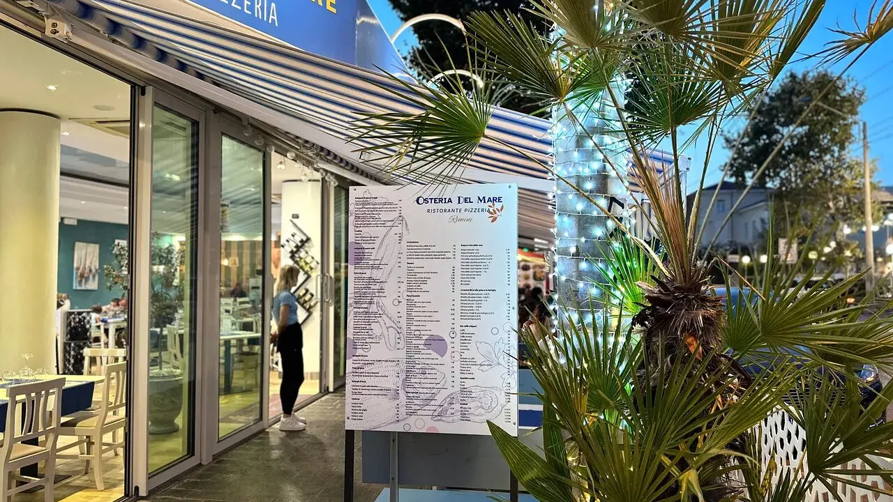 Osteria del Mare, ristorante pizzeria a Rimini centro, con menù esposto e tavoli all'esterno. Palme illuminate con lucine.