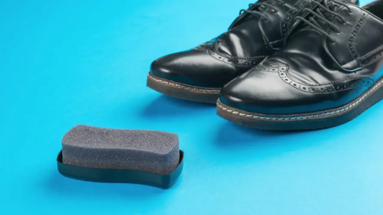 Czarne buty ze sztucznej skóry i gąbka do pastowania. Czy można pastować buty ze sztucznej skóry? Tak, specjalnymi preparatami.