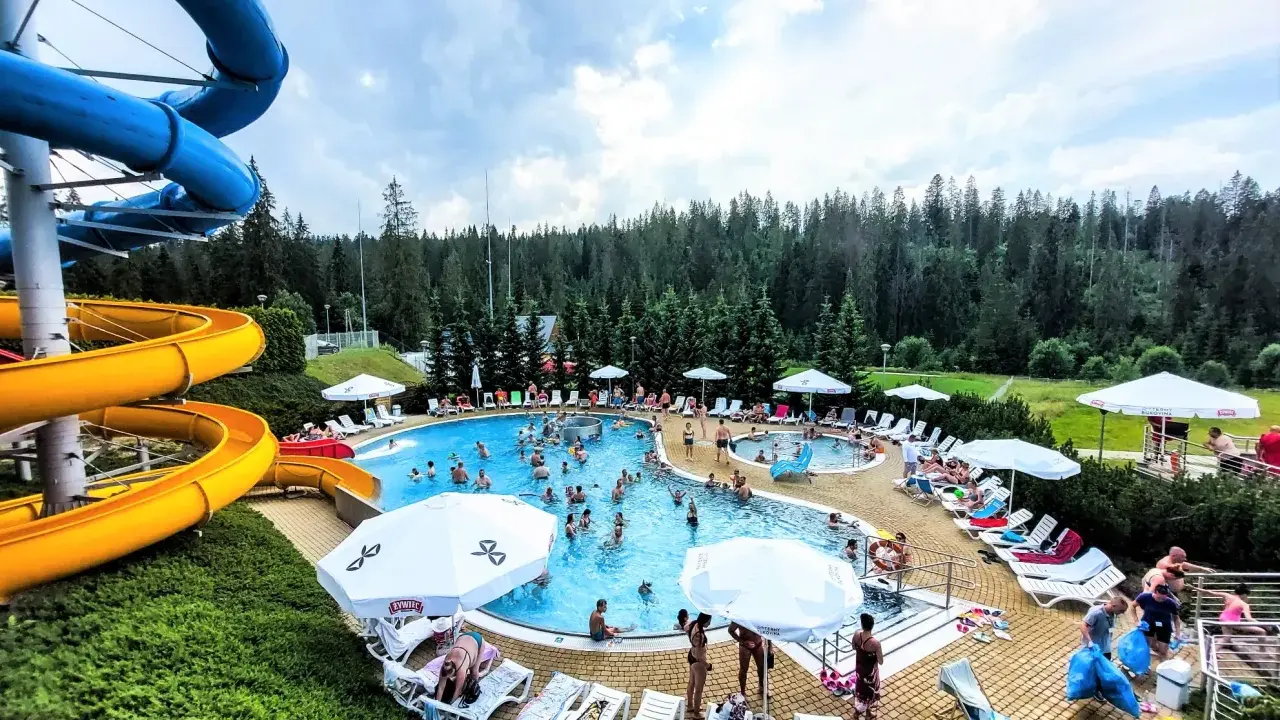 Aqua park Bukowina tętni życiem. Ludzie kąpią się w basenie, zjeżdżają ze zjeżdżalni i odpoczywają na leżakach.