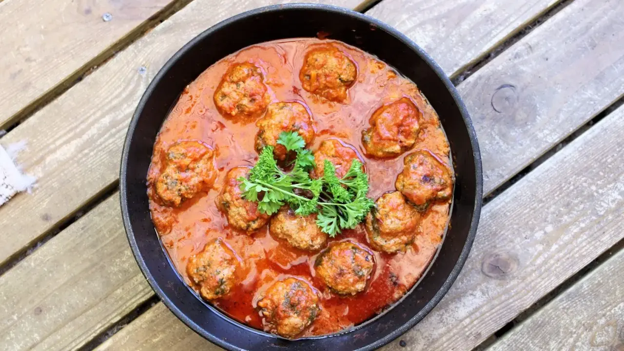 Frikadeller i tomatsås, en klassisk svensk rätt, serveras i en gjutjärnspanna. Garnerad med persilja.