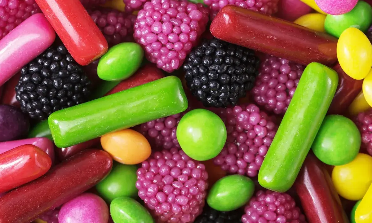 Dulces de colores vibrantes: gominolas, caramelos y pastillas. Se intuye que las gominolas están hechas de gelatina, azúcar y saborizantes frutales.