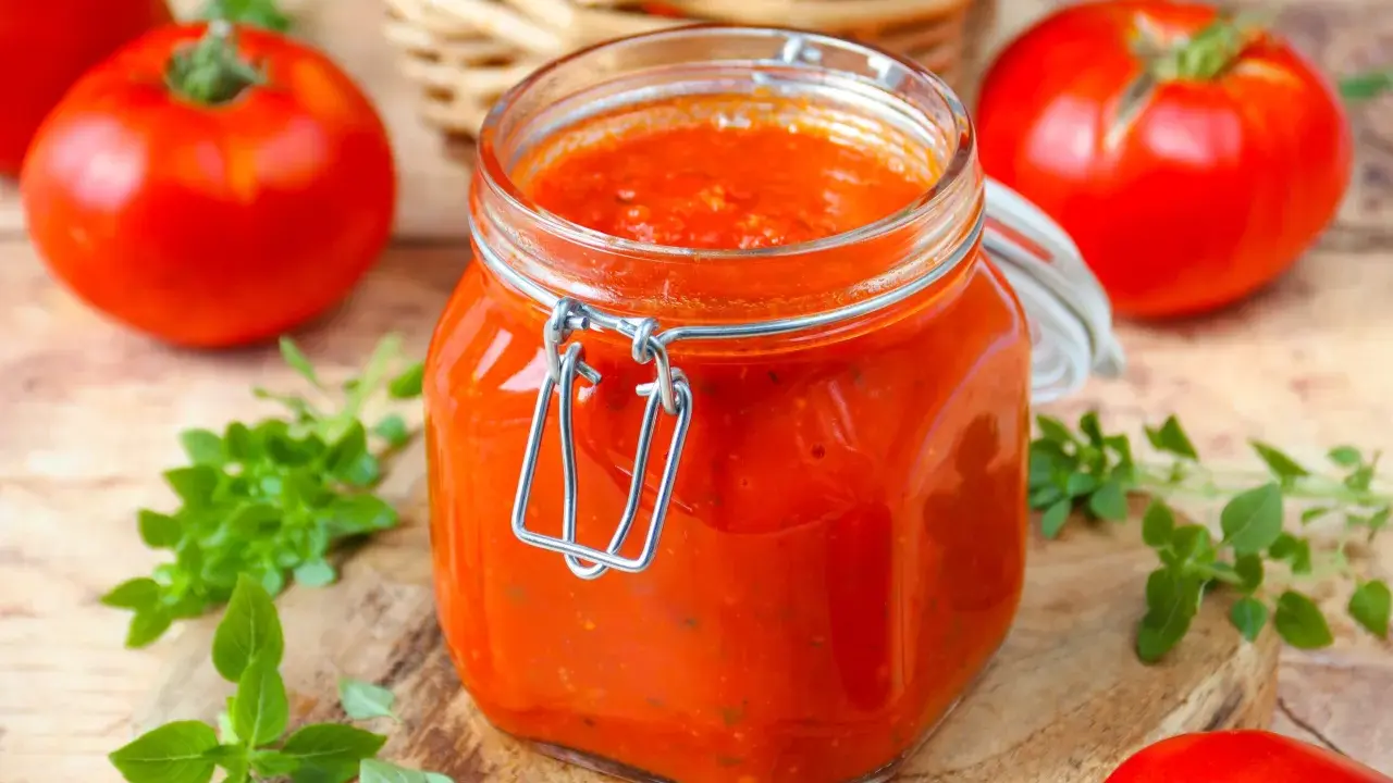 Un bocal de sauce tomate maison, avec des tomates fraîches et du basilic disposés autour.