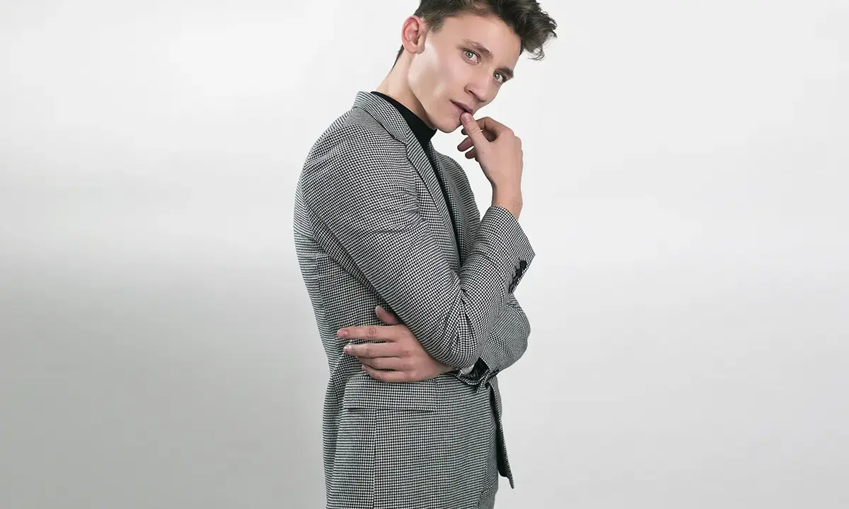 Elegancka stylizacja na 18 urodziny: młody mężczyzna w garniturze w drobną kratkę, czarny golf.