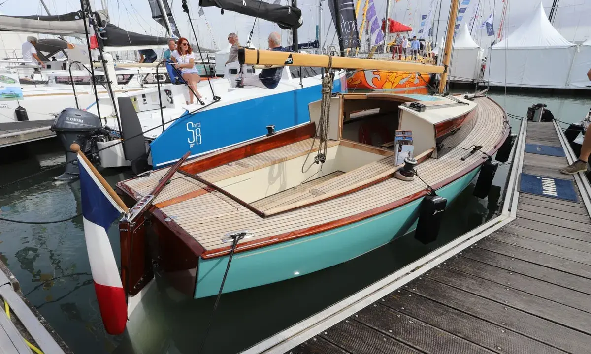Un élégant belouga bateau, aux finitions bois et coque turquoise, est amarré à quai.