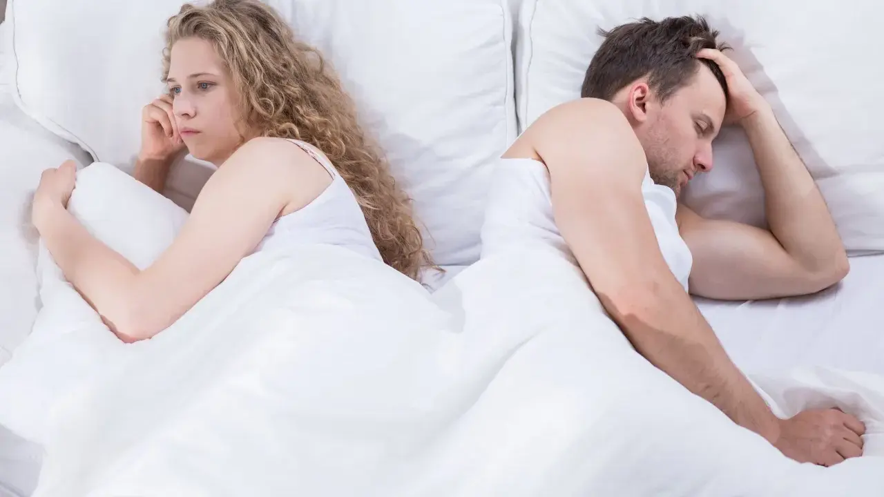 Para, odwróceni do siebie plecami w łóżku, zmartwiona kobieta i mężczyzna z ręką na czole. Czy to pochwica? Co to za problem?