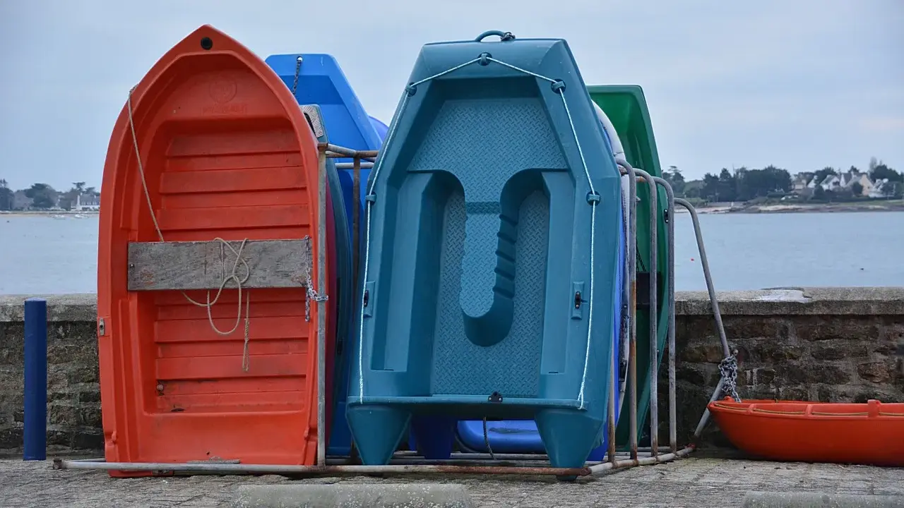 Plusieurs petites embarcations colorées, dont une annexe orange, sont rangées sur le quai, face à la mer.