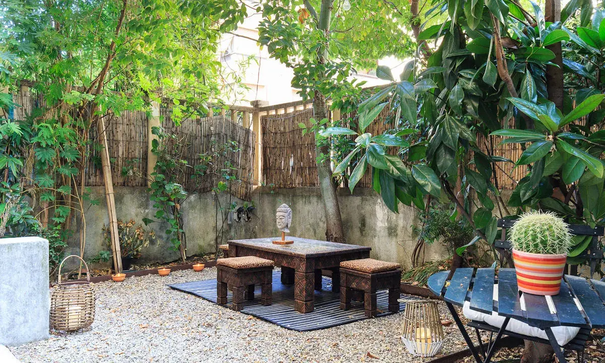 Un angolo relax per il tuo progetto giardino 50 mq: tavolino in legno intagliato, sgabelli, lanterne e un cactus vivace.