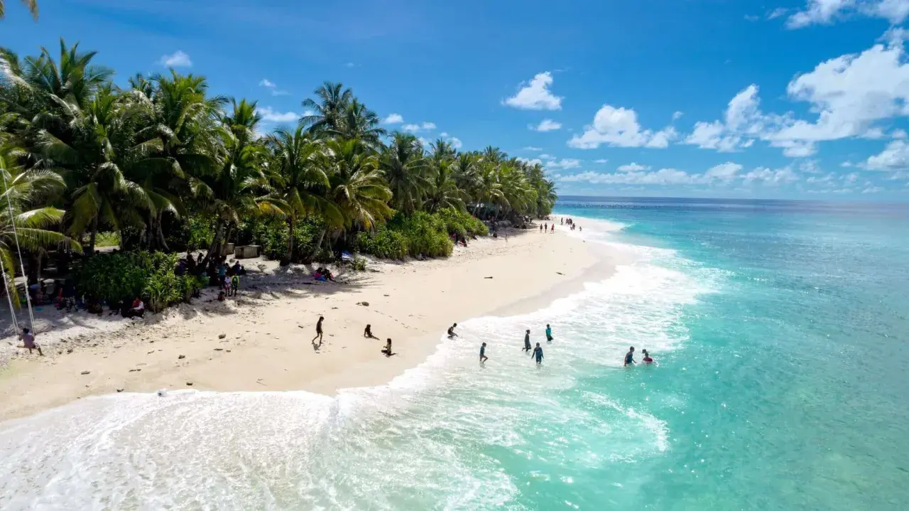 Spiaggia tropicale con palme e persone che nuotano nell'acqua cristallina dell'atollo di Maafushi.